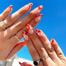 Close-up of hands with red and white floral nail design against a blue sky, Obroi