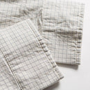 Two folded checkered fabrics with a grid pattern on a light background, Obroi
