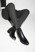 Black leather Chelsea boots worn with gray pinstripe pants on a white background, Obroi