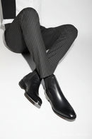 Black leather Chelsea boots worn with gray pinstripe pants on a white background, Obroi