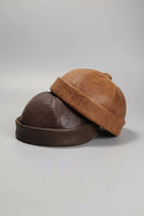 Two brown leather hats stacked on a dark background with a black handbag, Obroi