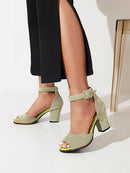Green high-heeled shoes worn with a black outfit on a light background, Obroi