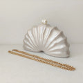 Shell-shaped clutch with a gold chain on a light gray background, Obroi