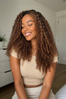 Woman with curly hair smiling in a room with a white door and plant, Obroi