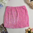 Pink sequin skirt on a light gray surface with flowers around, Obroi