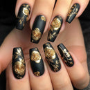 Black nails with gold floral designs on a hand, Obroi