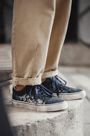 Close-up of navy sneakers with leopard print details worn with beige pants on a concrete surface, Obroi