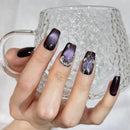 Hand with dark purple nail polish holding a clear glass mug, Obroi