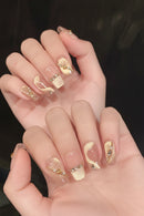 Hand with gold and clear nail design on a dark background, Obroi