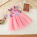 A toddler girl's sleeveless tulle dress with a pink mesh skirt and a purple floral bodice, styled on a white sheet with a beige blanket, a book, and small flowers, Obroi