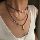 Necklace with blue beads and gold accents worn by a person in a white top, Obroi