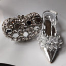 Silver heart-shaped clutch and high-heeled shoe with floral details on a white background, Obroi