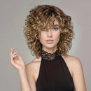 Woman with styled hair holding a hair product against a neutral background, Obroi