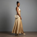 Woman in a gold dress holding a matching handbag against a gray background, Obroi