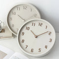 Two round wall clocks on a white surface with books and a mug in the background, Obroi