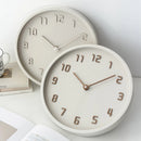 Two round wall clocks on a white surface with books and a mug in the background, Obroi