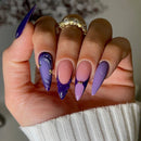 Hand with purple and pink nail design wearing a gold ring, blurred background, Obroi