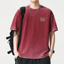 Person wearing a maroon t-shirt with a logo, black pants, and a black backpack on a light gray background, Obroi