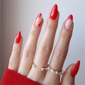 Close-up of a hand with red and pink nail polish wearing two rings on a neutral background, Obroi