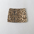 A leopard print sequin mini skirt with black and brown spots on a beige background, laid flat against a light gray textured wall, Obroi