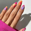 A close-up of a hand with colorful, stylized almond-shaped nail art. The nails feature gradients and abstract designs in pink, orange, purple, yellow, and white, with a bright pink sleeve visible at the bottom left against a neutral gray background.