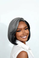 A smiling woman wearing a short, layered bob wig with gray and black ombre styling, paired with a white collared shirt against a clean light gray background, Obroi