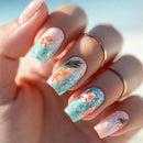 Nails with tropical design featuring palm trees and flowers, held against a blurred natural background, Obroi