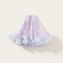 A sleeveless tiered tulle dress in soft lavender and pale blue, featuring a ruffled floral hem, displayed on a warm cream background, Obroi