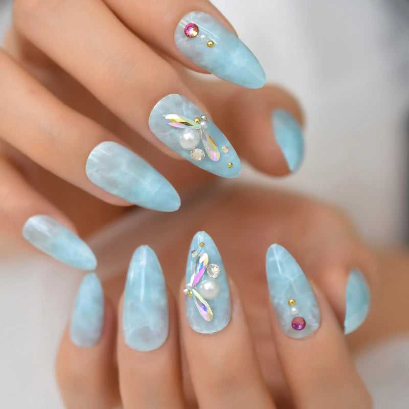 Light blue nail polish with decorative elements on a hand against a neutral background, Obroi