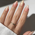 Obroi Hand with gold nail polish and a gold ring on a neutral background