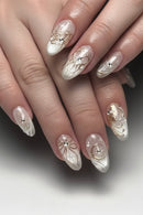 Close-up of manicured fingernails with a glossy white and silver floral design, gold metallic swirls, and small clear rhinestone accents on a hand, Obroi
