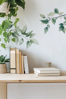 Books on a wooden shelf with plants and a white wall in the background, Obroi