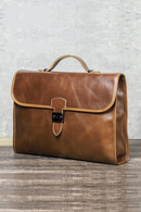 Brown leather briefcase on a wooden surface with a gray textured wall background, Obroi