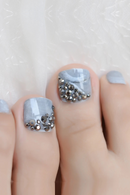 Toe nails with gray nail polish and decorative rhinestones on a white background, Obroi