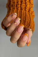 Close-up of a hand with orange and pink nail polish wearing a textured orange sweater, Obroi