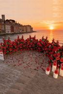 Decorative setup with red flowers and candles by the sea at sunset, Obroi