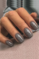 Close-up of a hand with glittery gray nail polish on a textured surface, Obroi