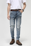 Person wearing light blue jeans with visible distressing, a white t-shirt, brown belt, and brown boots on a plain background, Obroi