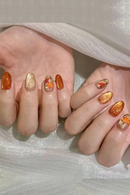 Close-up of hands with orange and gold nail polish on a light background, Obroi