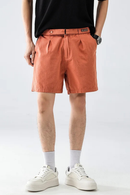 Person wearing orange shorts and white sneakers on a plain background, Obroi