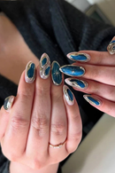Close-up of hands with blue and silver nail designs against a blurred background, Obroi