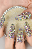 Close-up of a hand with rhinestone nail art on a textured surface, Obroi