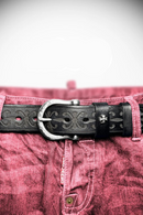 Close-up of a black leather belt with decorative buckle on pink denim, Obroi