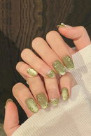 Close-up of a hand with green glittery nail polish on a wooden surface, Obroi