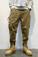 Person wearing brown cargo pants and yellow boots against a white wall, Obroi