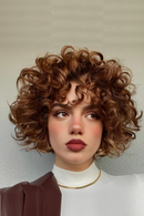 Woman with curly brown hair wearing a white top and gold necklace against a plain background, Obroi