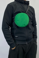 Person wearing a black jacket with a green round bag on a white background, Obroi
