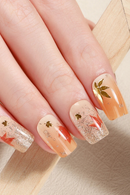 Close-up of a hand with peach-colored nails featuring gold leaf designs on a neutral background, Obroi