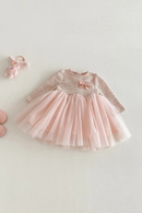 A baby girl's long-sleeve dress with a textured light beige knit top, a pink bow at the chest, and a layered light pink tulle skirt, laid flat on a light gray background, Obroi