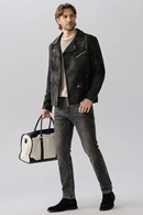 Man wearing a black leather jacket and gray jeans, holding a black and white bag on a light gray background, Obroi